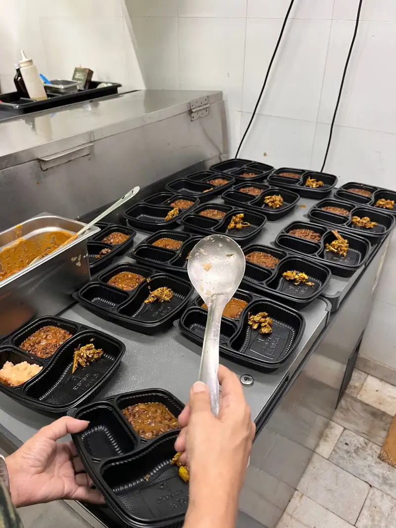 Rows of open meal trays being filled from a serving ladle